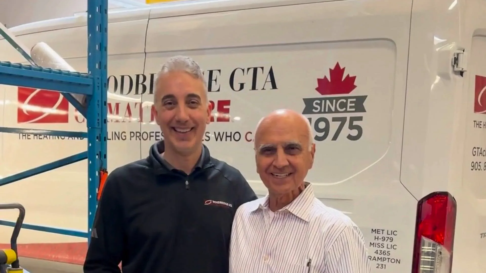 Two men posing in front of a branded vehicle.