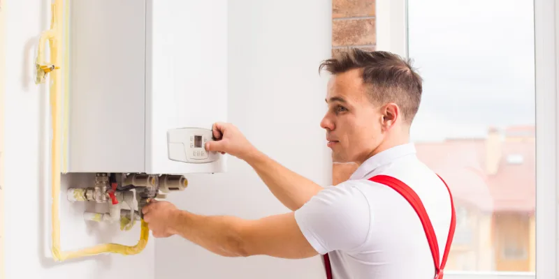 A technician adjusting a boiler control panel in an interior setting.