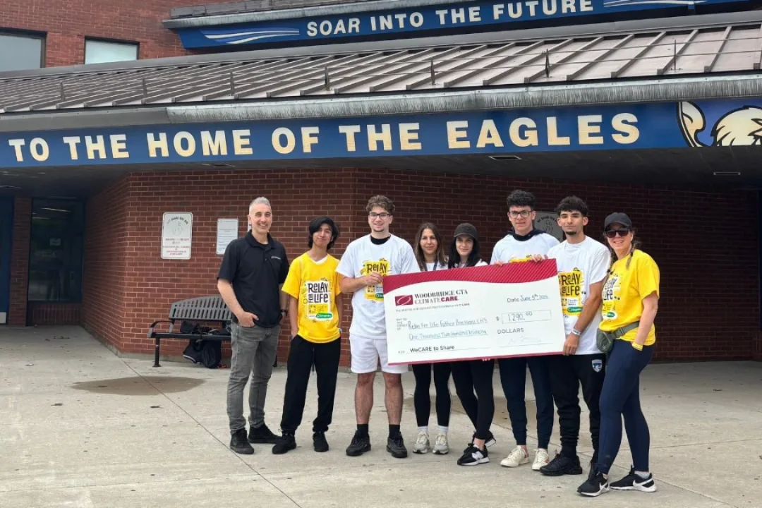 Students holding a donation check in front of a school building.