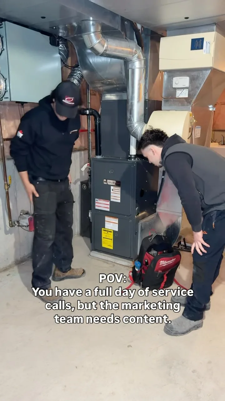 Two HVAC technicians examining a furnace in a service area.
