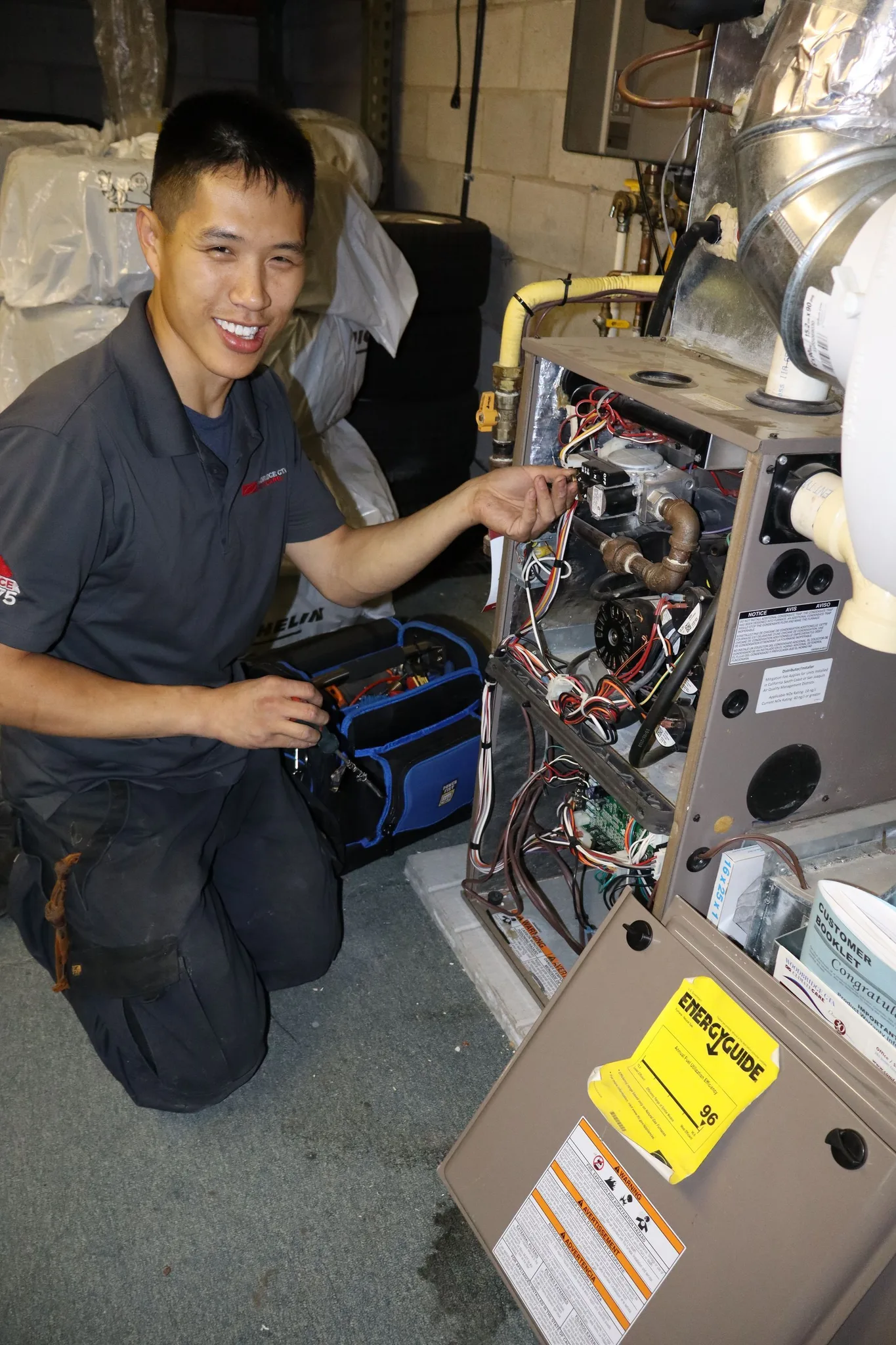 A smiling HVAC technician working on a furnace in a basement.