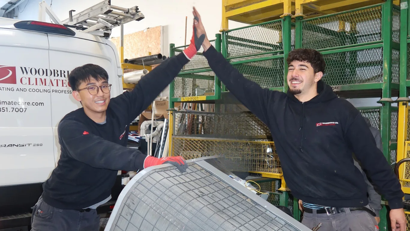 Two technicians giving a high-five in an HVAC workshop.