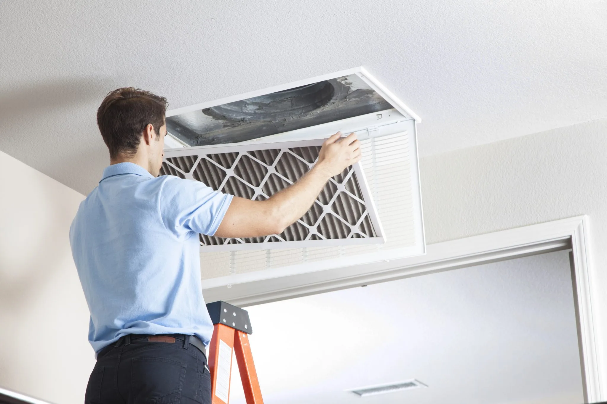 Technician replacing an air filter in a ceiling HVAC unit.