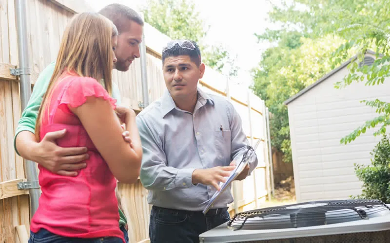 A technician provides air conditioning maintenance guidance to a couple.