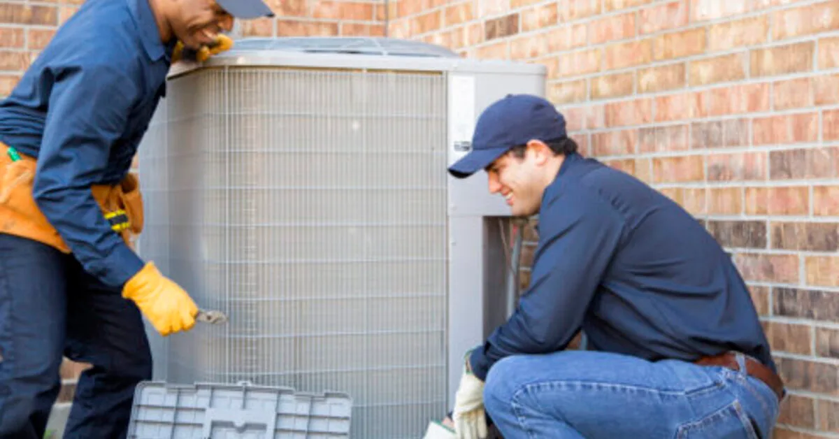 Two HVAC technicians servicing an outdoor unit.