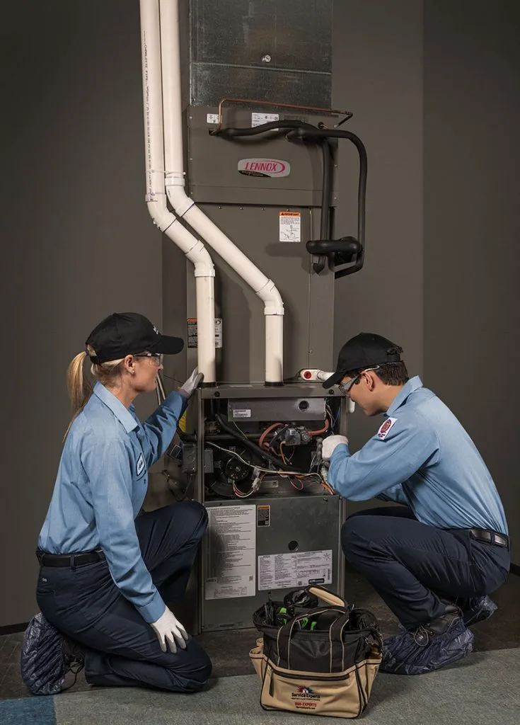 Two HVAC technicians working on a Lennox furnace