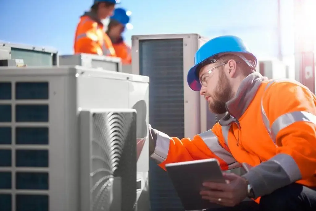 Technician inspecting an air conditioning unit with a tablet.
