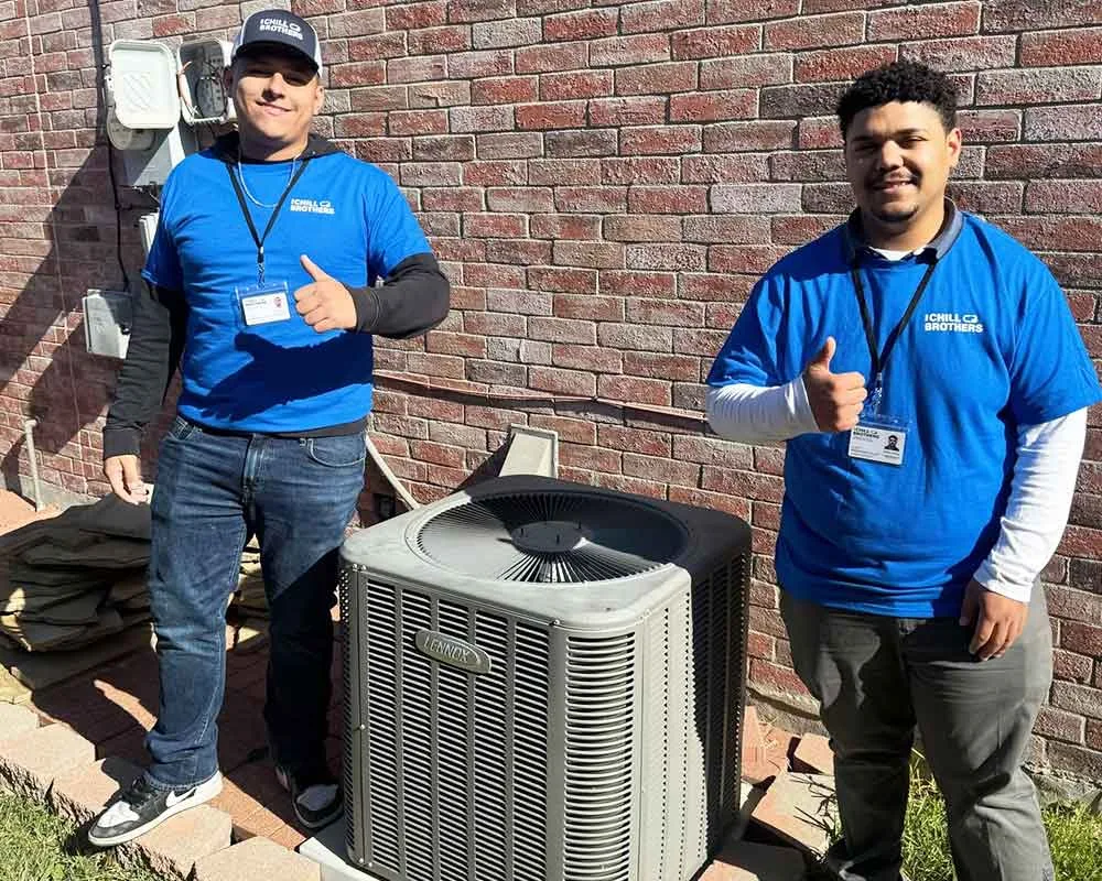 Two HVAC technicians posing with an air conditioning unit.