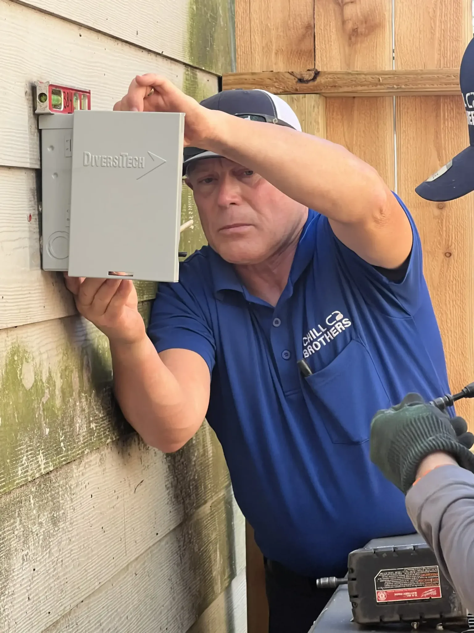 Technician installing a control box on an exterior wall.