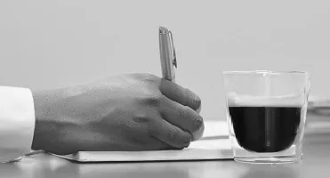 A hand writing in a notebook with a cup of coffee nearby.