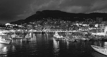 A nighttime harbor view with boats and city lights.