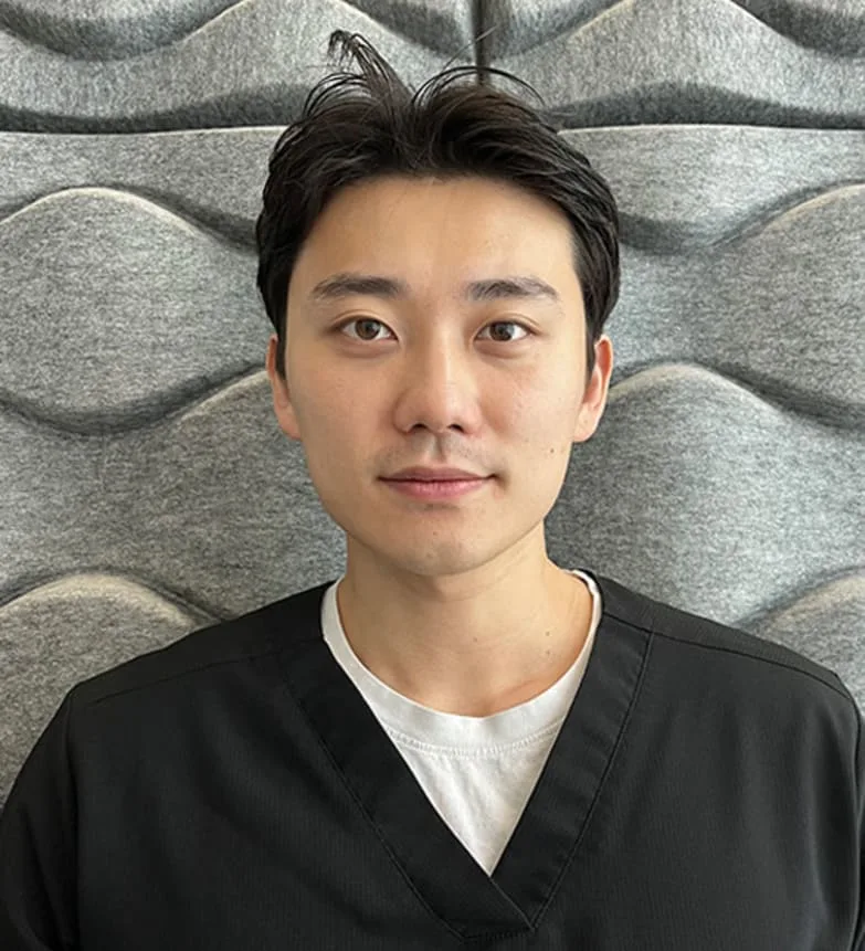 A young male dentist in black scrubs.