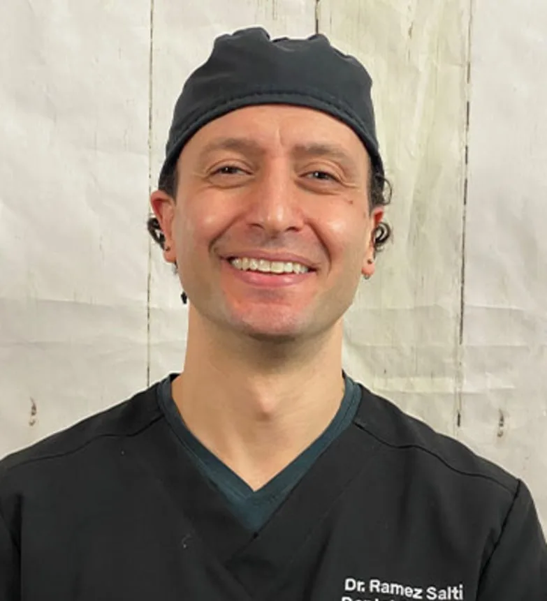 Smiling dentist in black scrubs and cap.