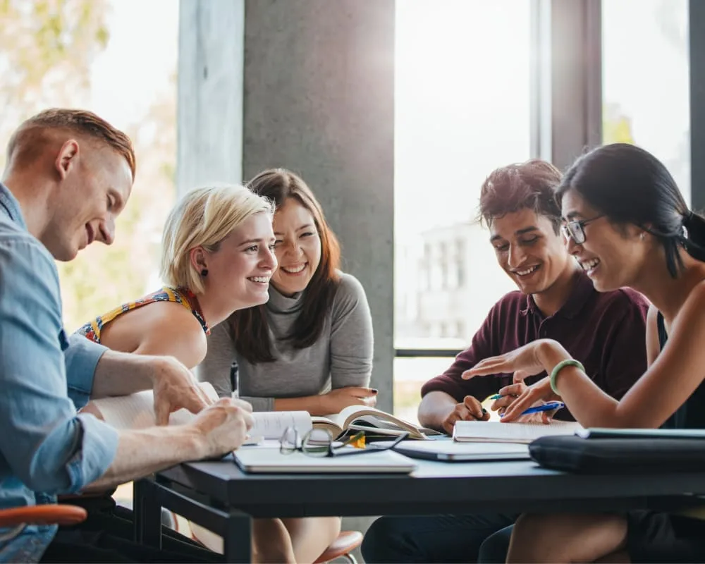 Five people collaborating at a table with notebooks and pens.