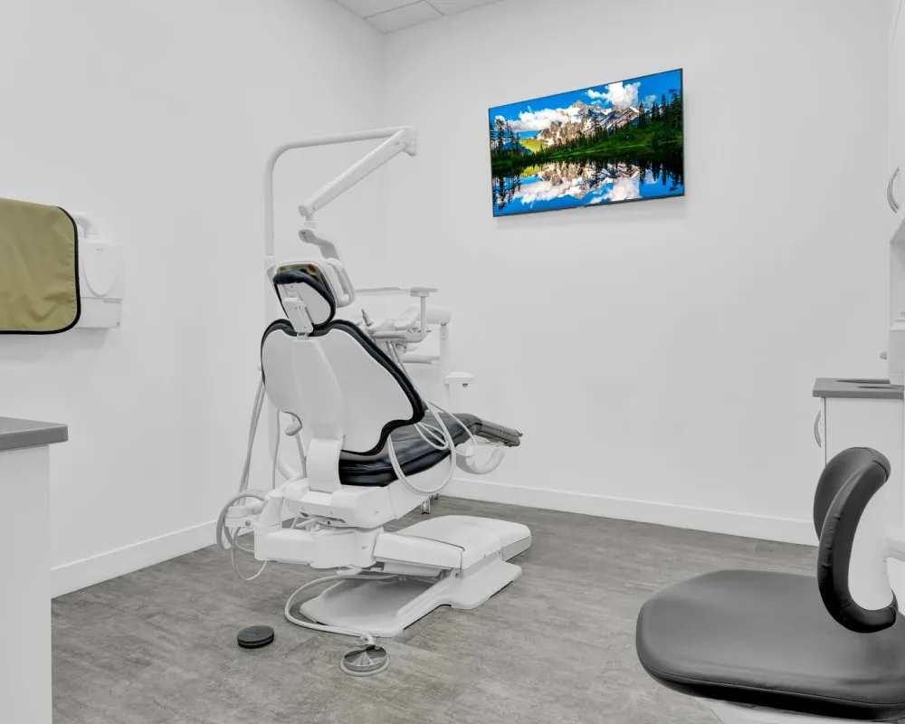 A modern dental treatment room with a dental chair and a TV.