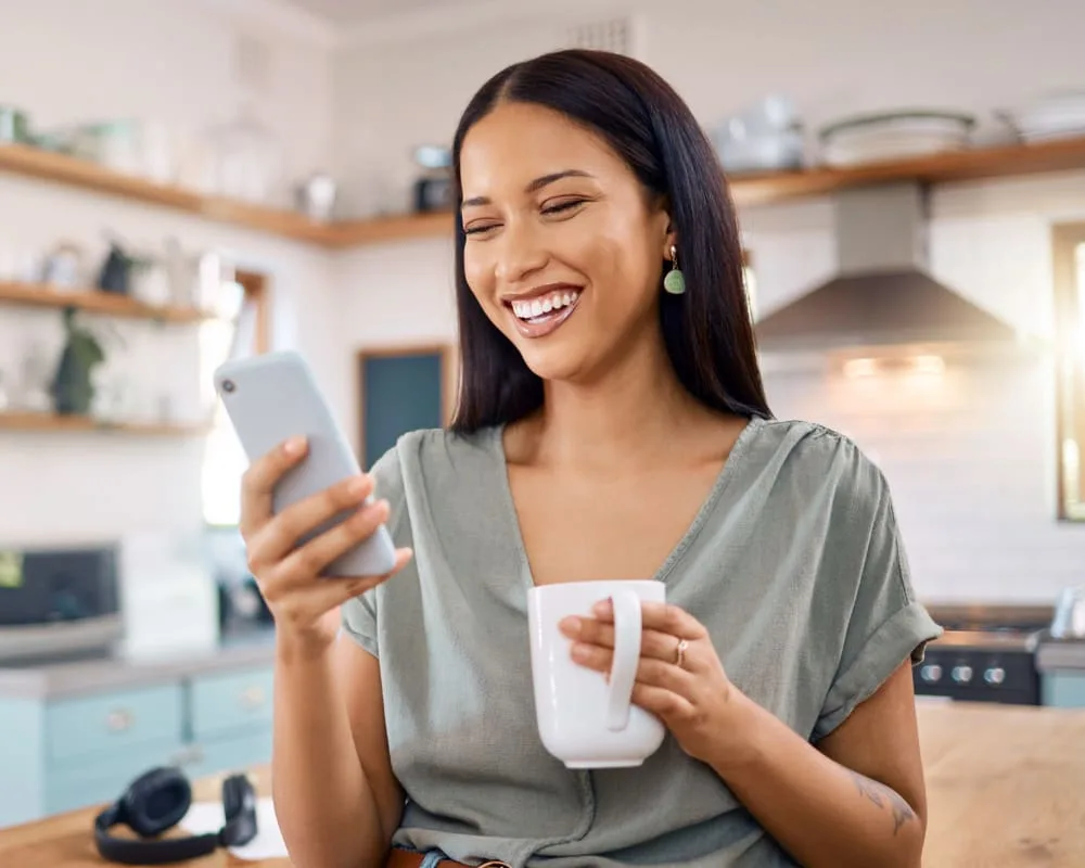 Young woman smiling at her smartphone in a kitchen.