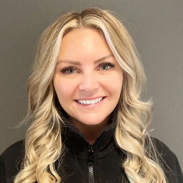 A woman smiling in a black jacket against a gray background.