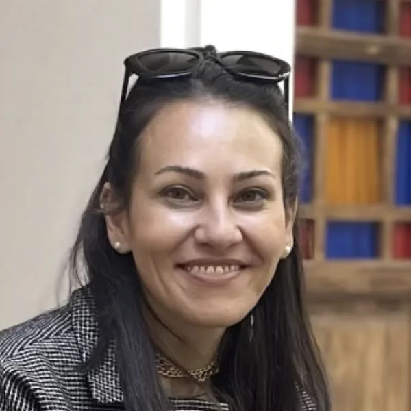 A smiling woman wearing a blazer and sunglasses.