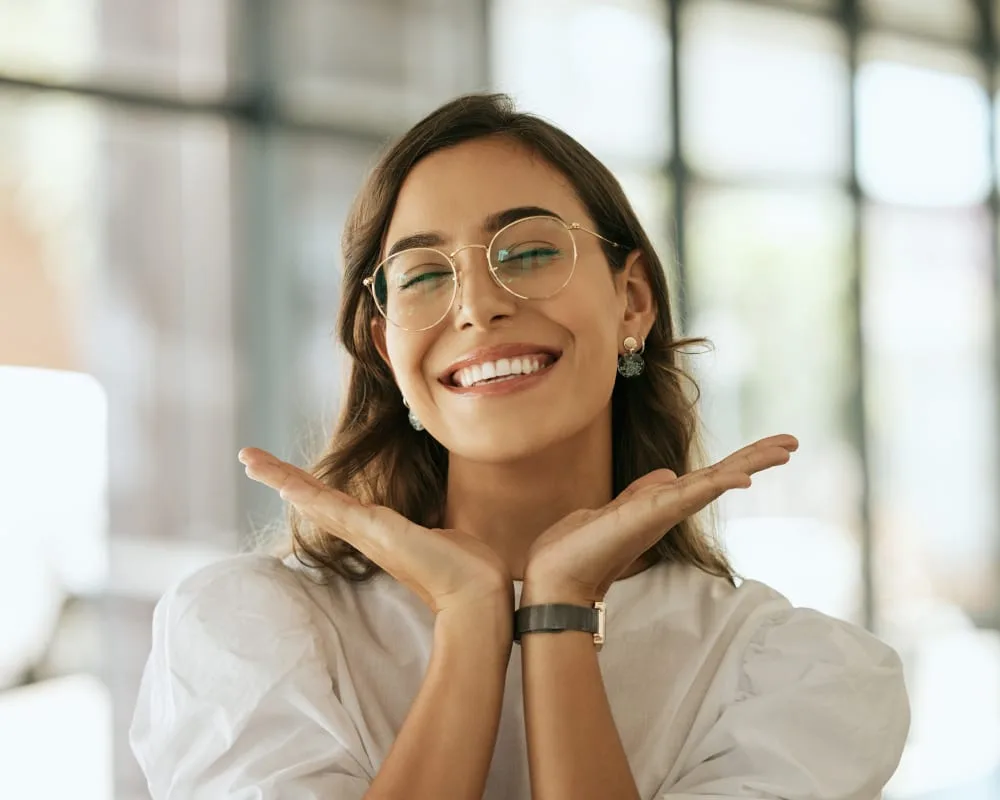 A smiling woman with glasses posing happily in a modern setting.