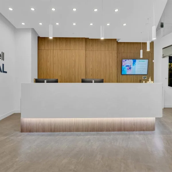 A modern dental reception area with a white desk and wood paneling.