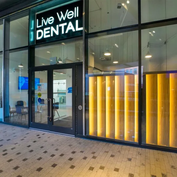 Entrance of Live Well Dental with glass facade and wooden accents.