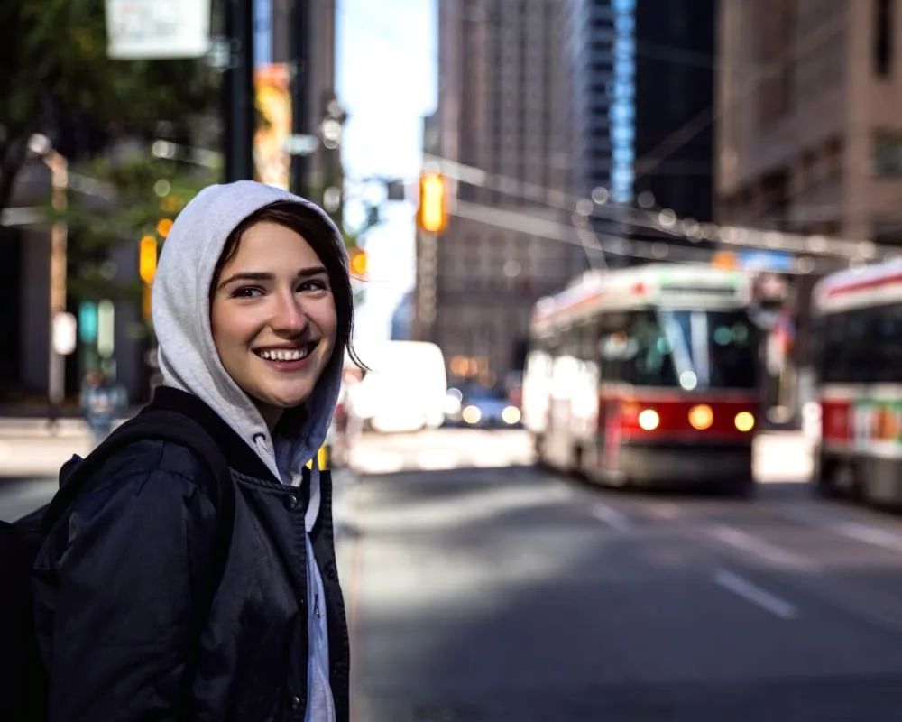A smiling young woman on a city street with a streetcar.