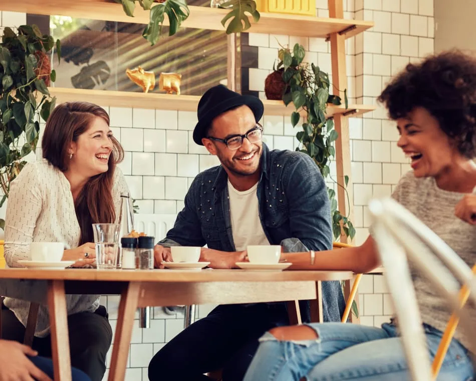 Three friends laughing together at a café table.