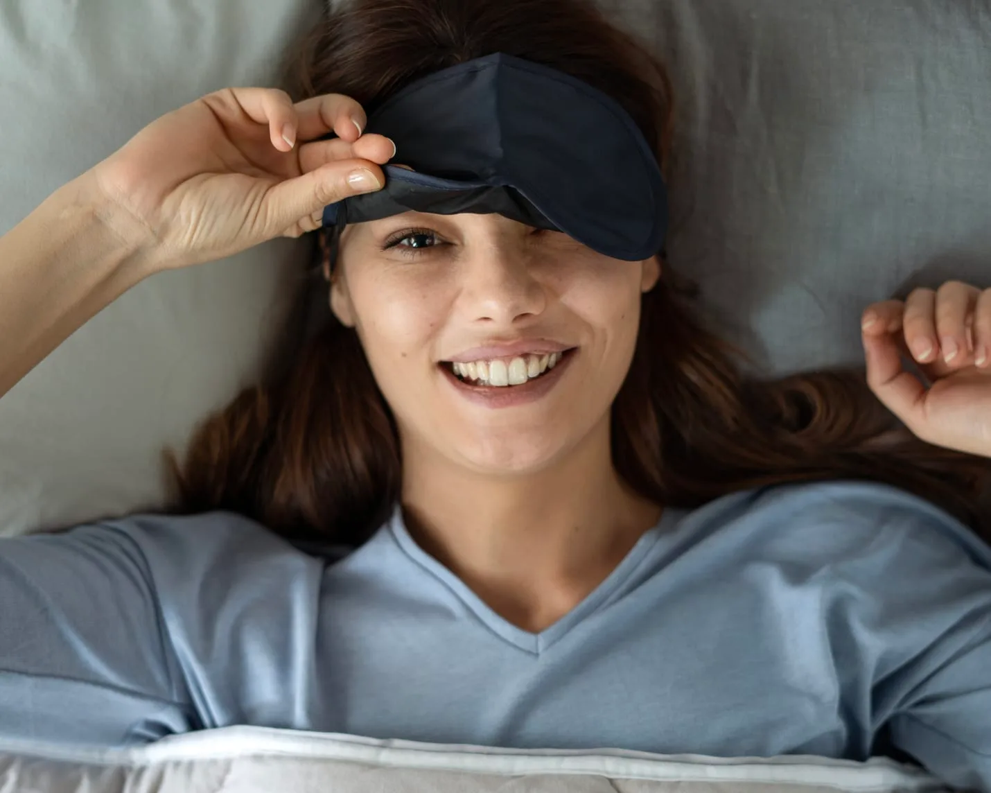 A smiling woman with a sleep mask in bed.