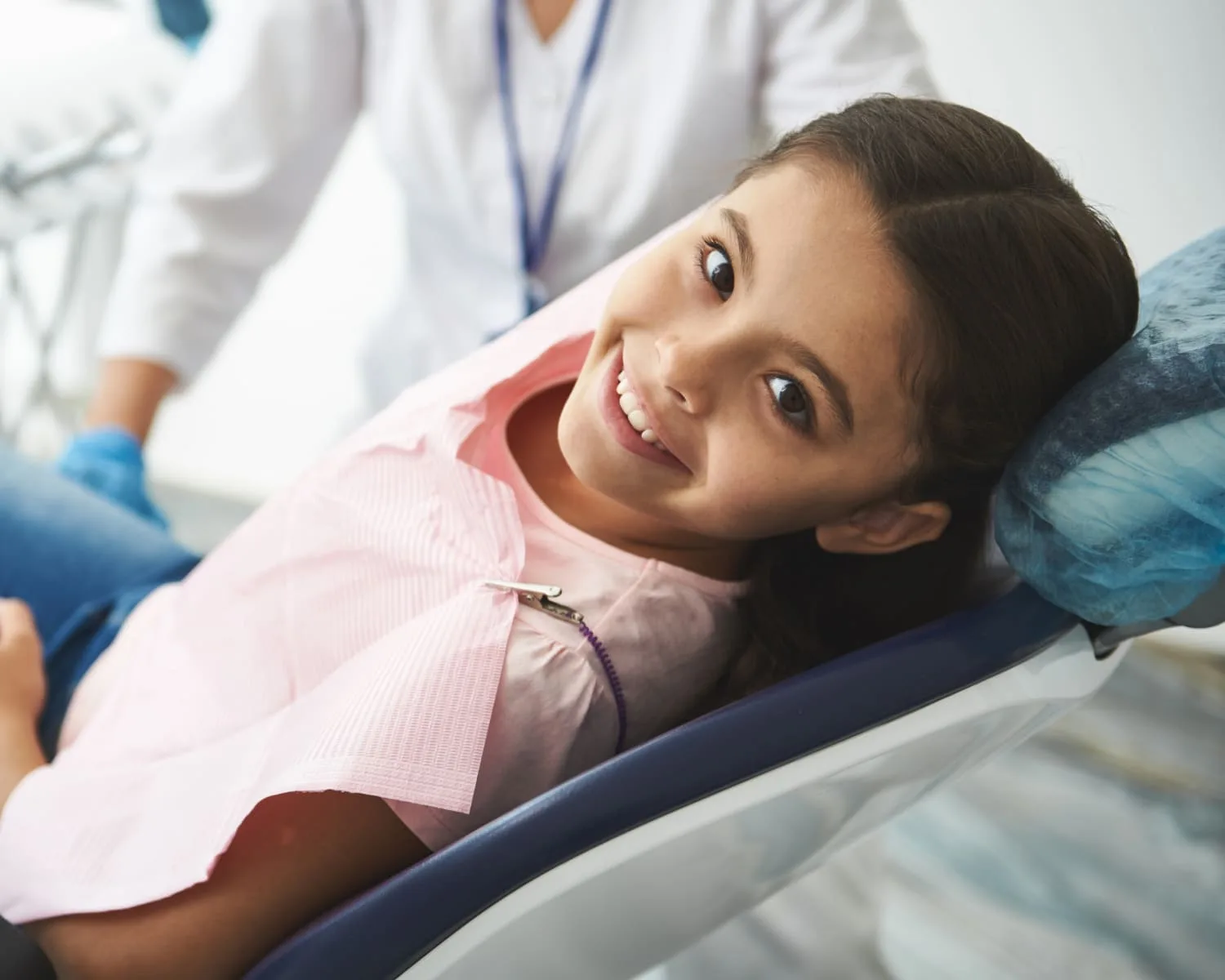 A girl smiling in a dental chair with a professional nearby.