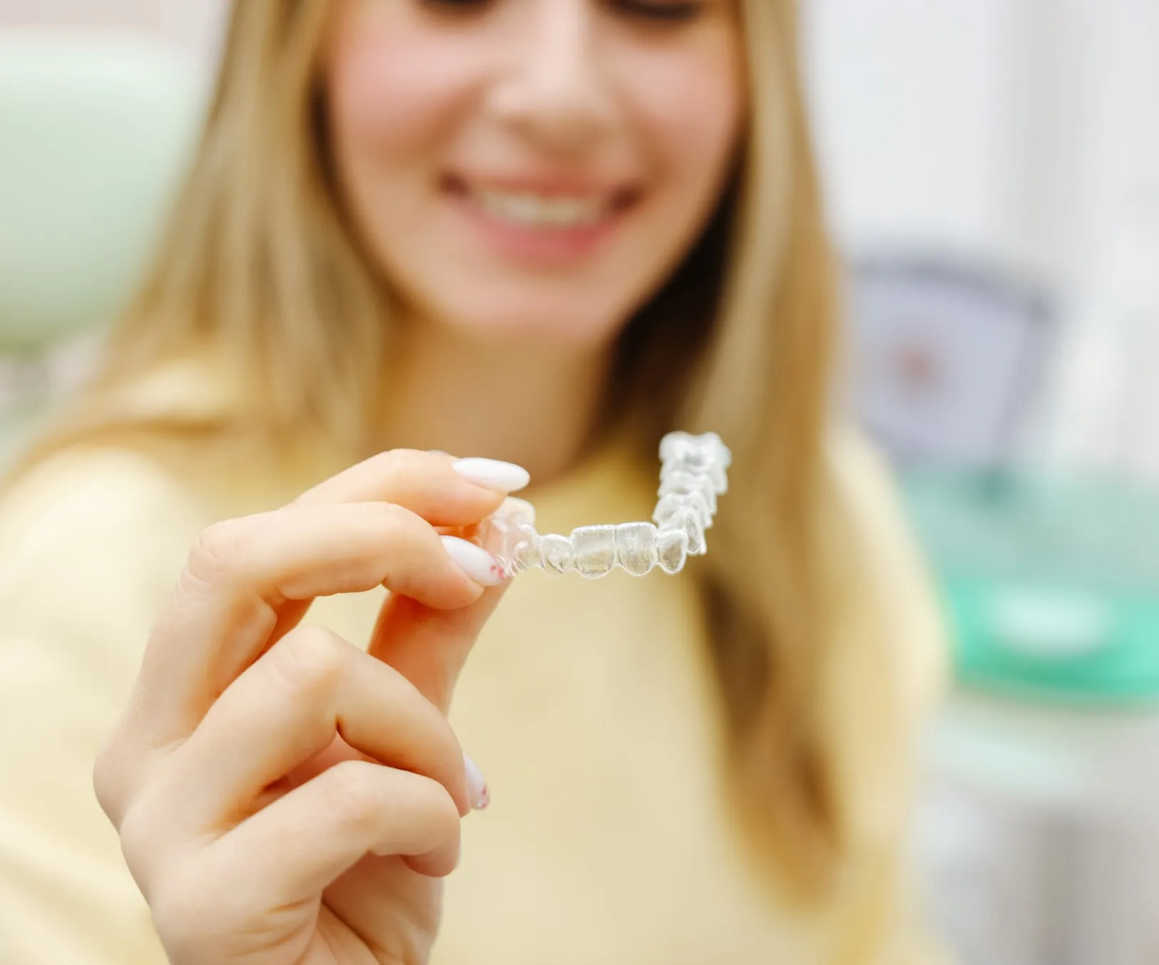 A woman holding a clear dental aligner and smiling.