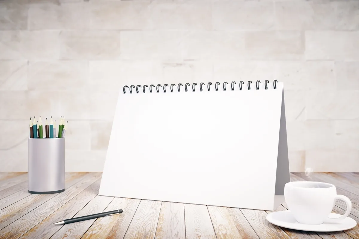 A blank notepad with a coffee cup and pens on a table.
