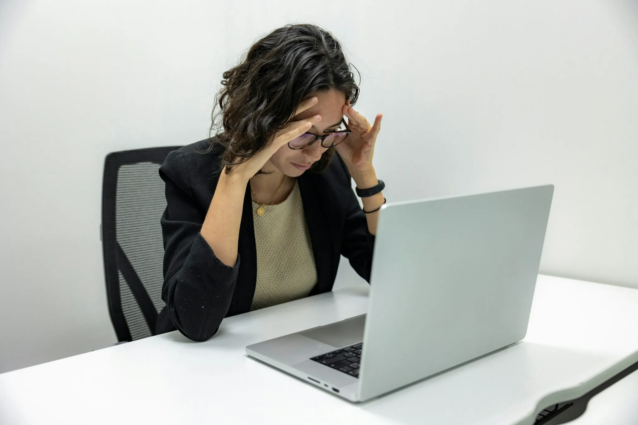 A woman appearing stressed at her desk with a laptop.