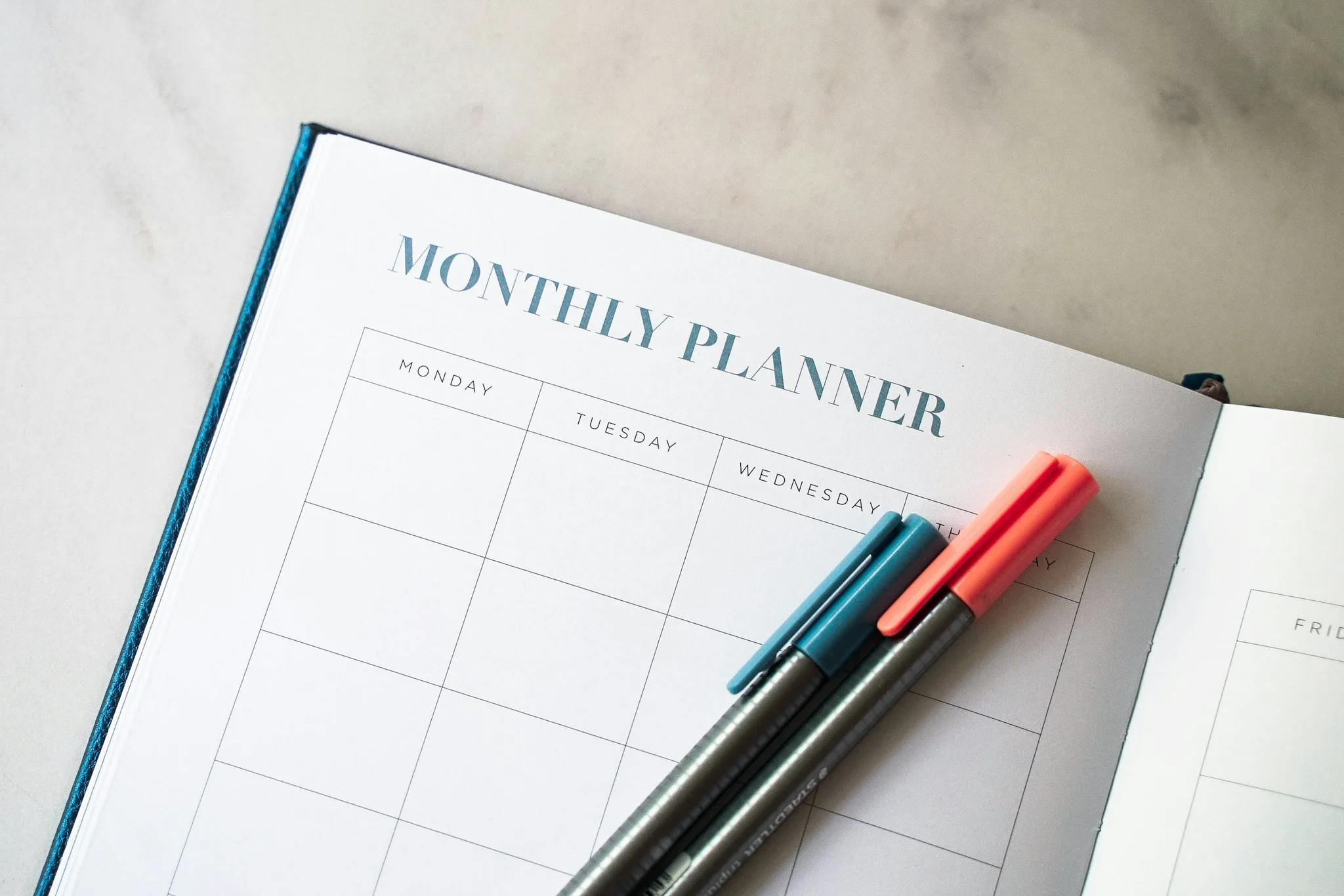 Open monthly planner with colored pens on a marble surface.