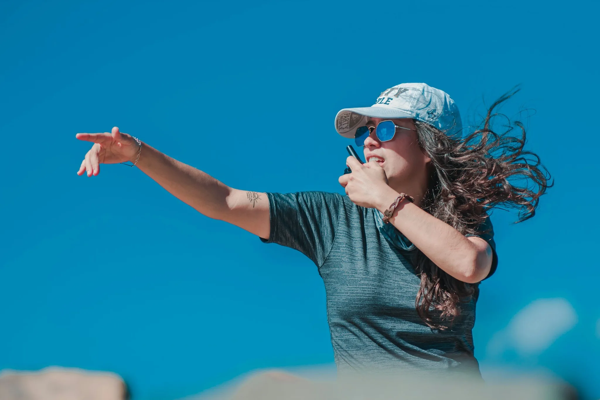 A woman gesturing confidently outdoors against a blue sky.