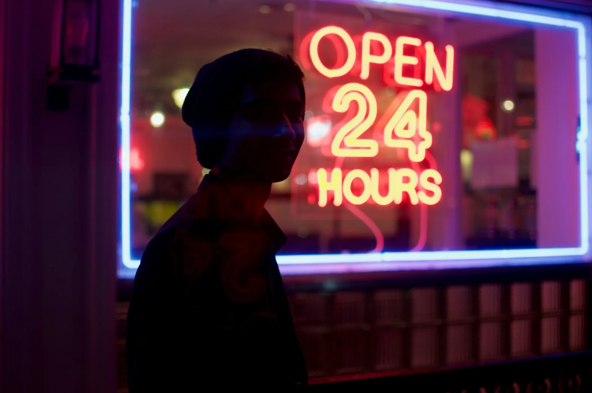 Silhouette in front of a neon 'OPEN 24 HOURS' sign.