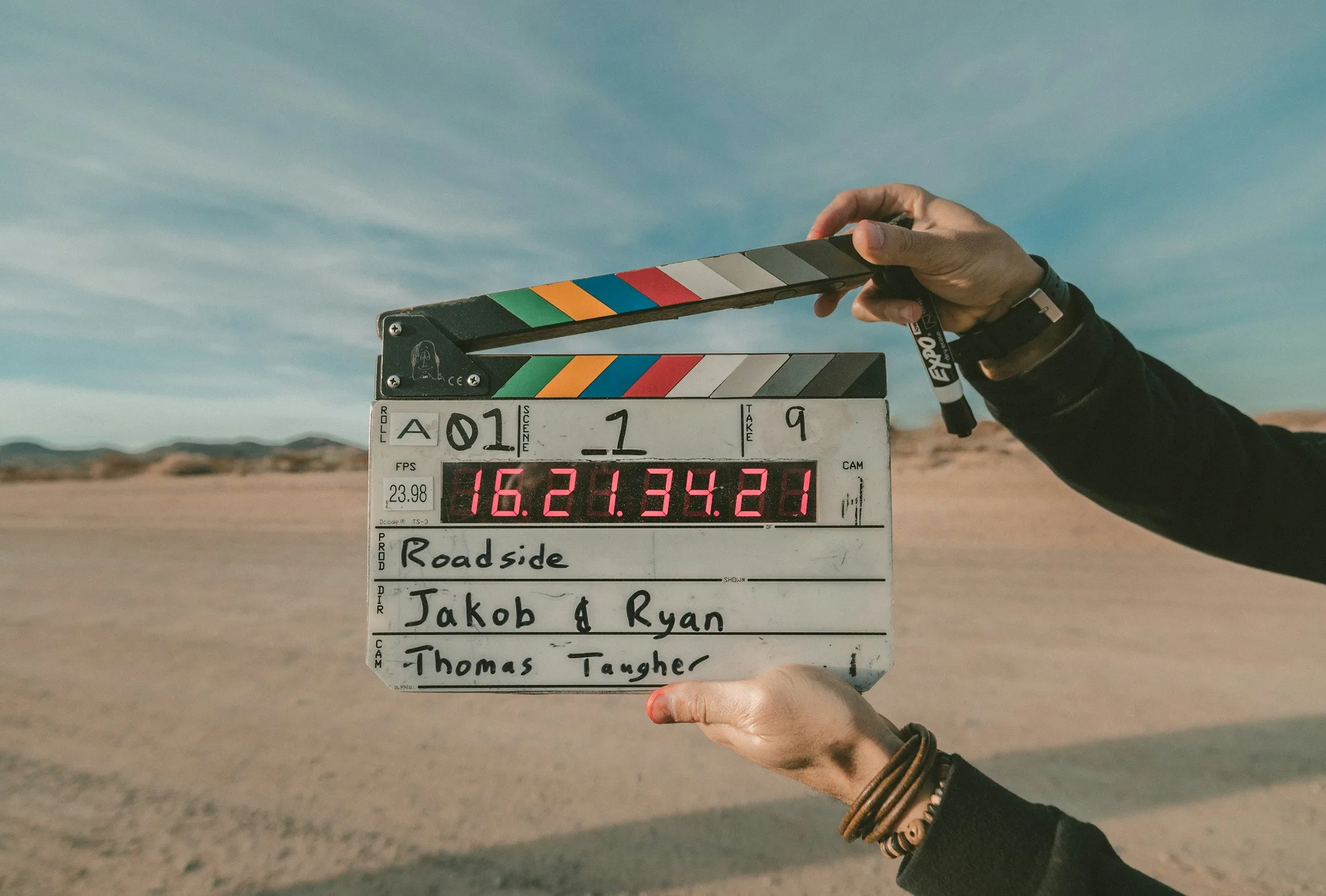 A person holds a clapperboard in a desert area.