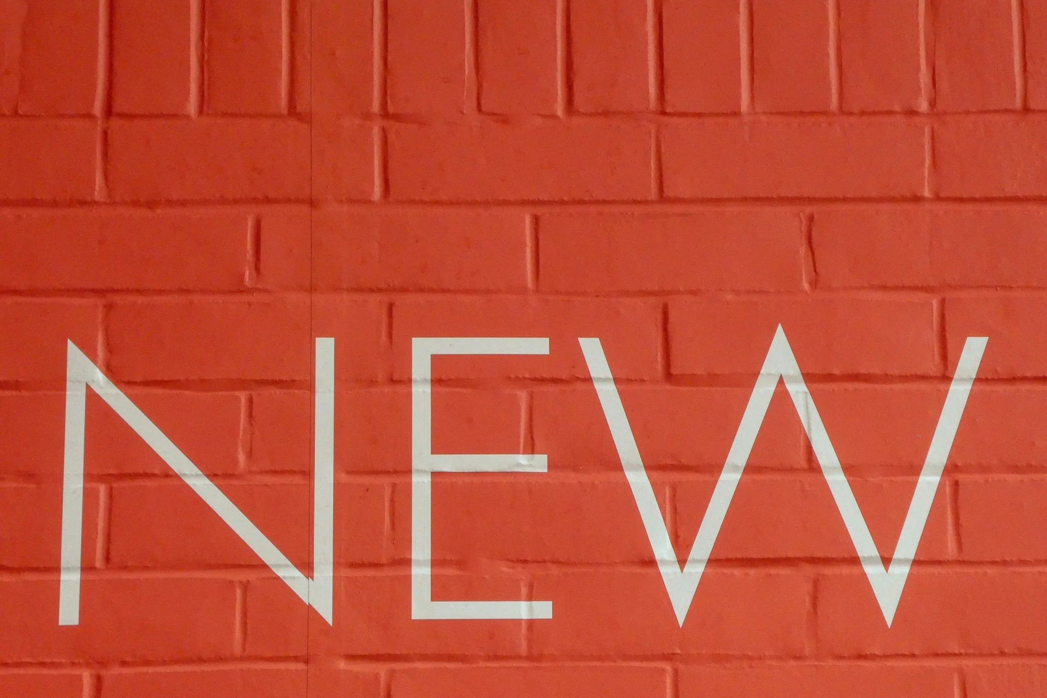 The word 'NEW' on an orange brick wall.
