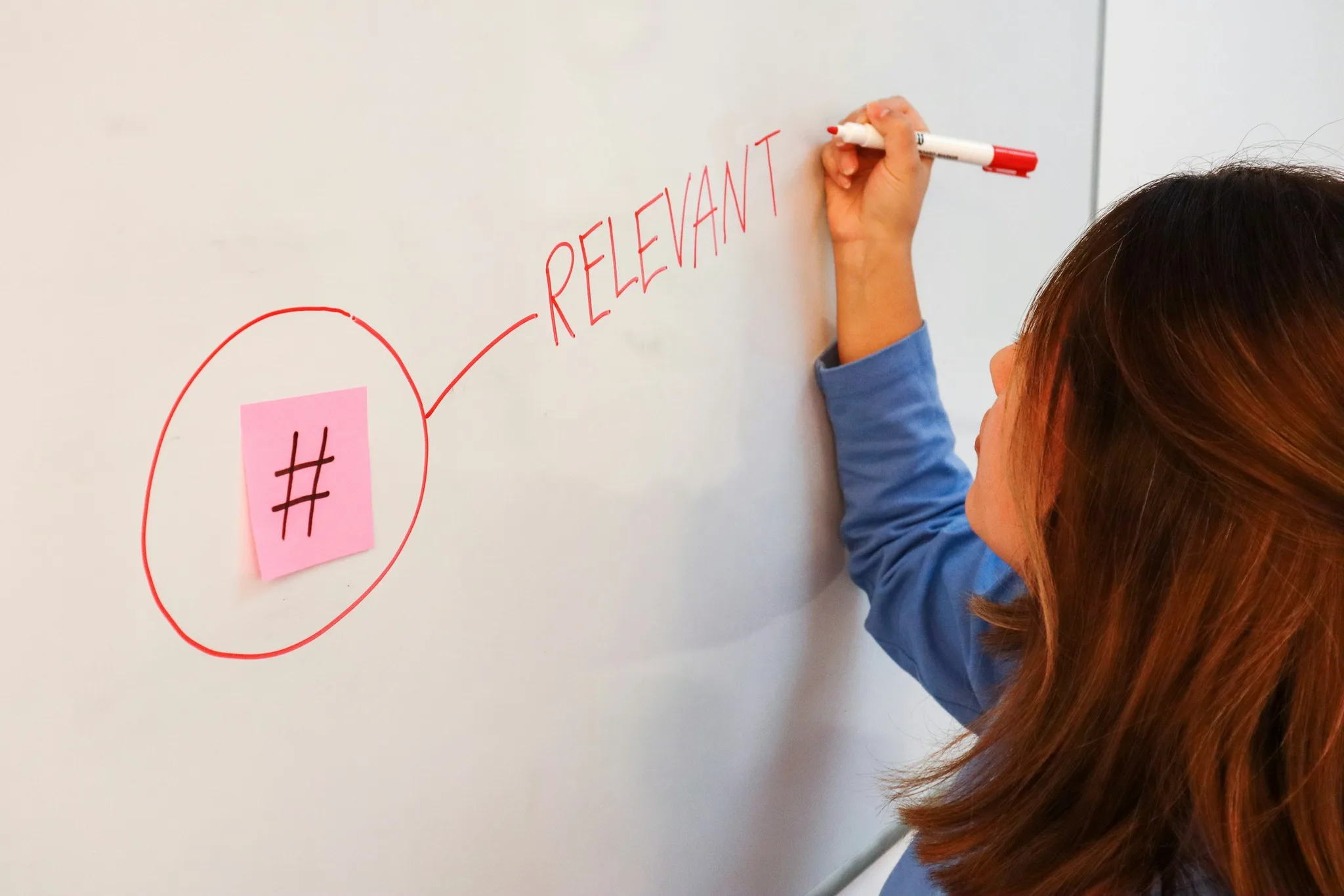 A woman writing 'RELEVANT' on a whiteboard.