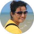 A woman smiling by the beach in sunglasses.