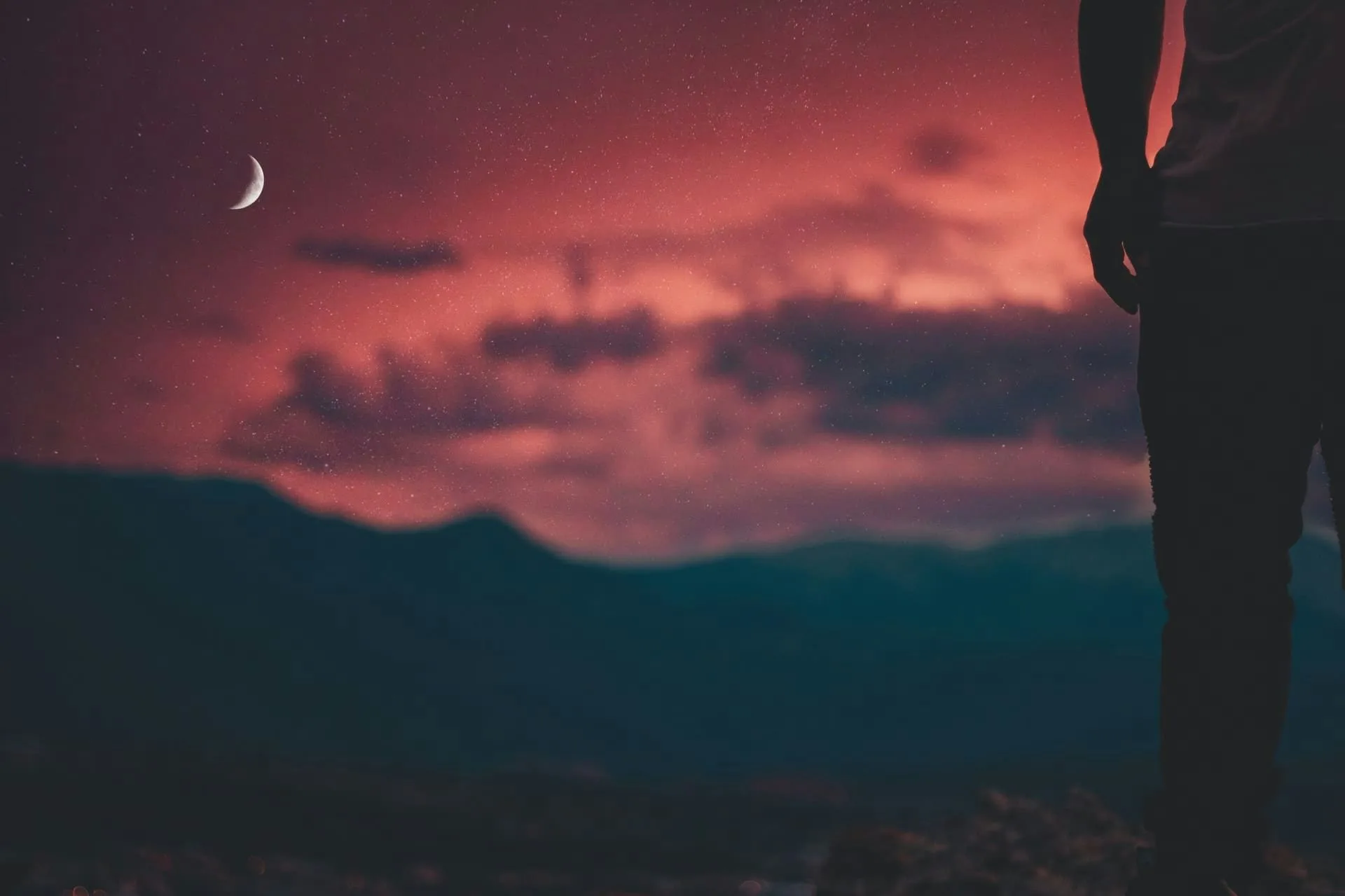 A person silhouetted against a colorful sunset and crescent moon.