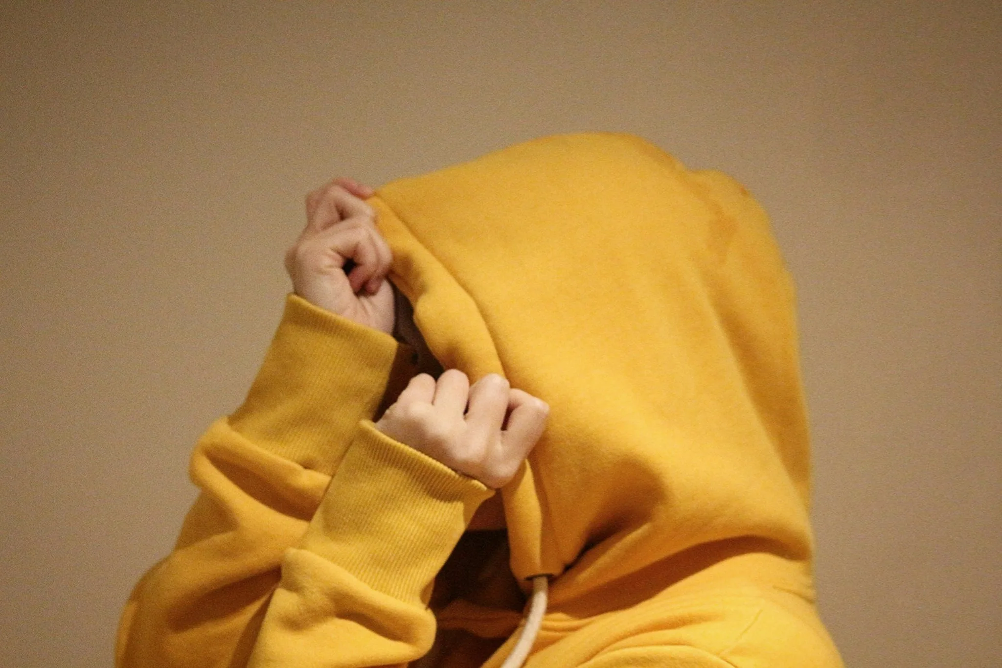 Person in a yellow hoodie covering their face with hands.