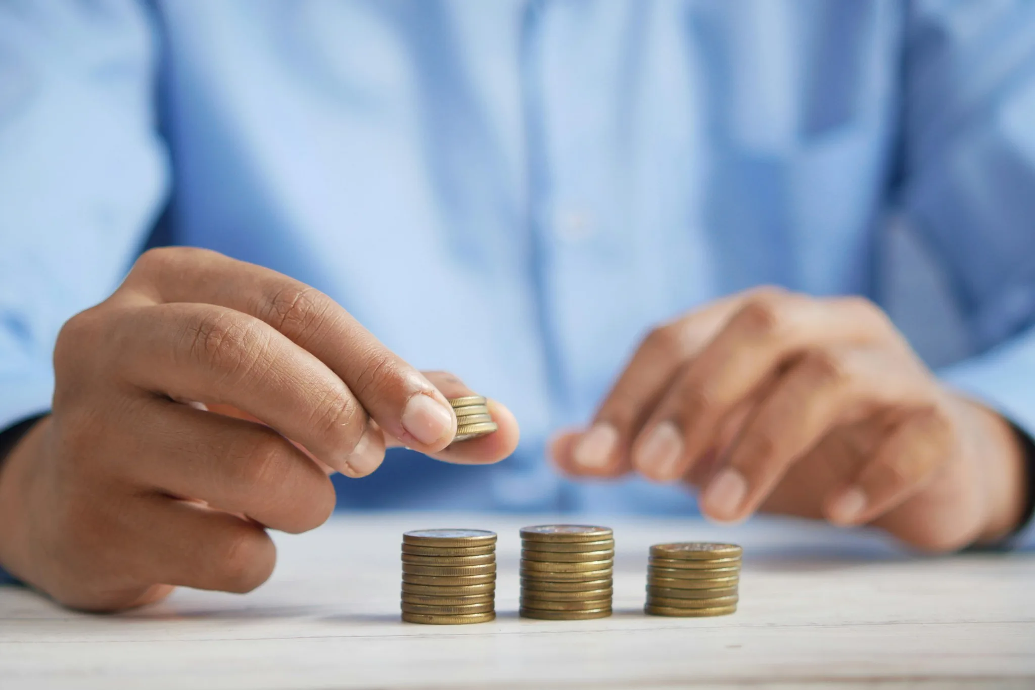 Hands stacking gold coins on a wooden surface.