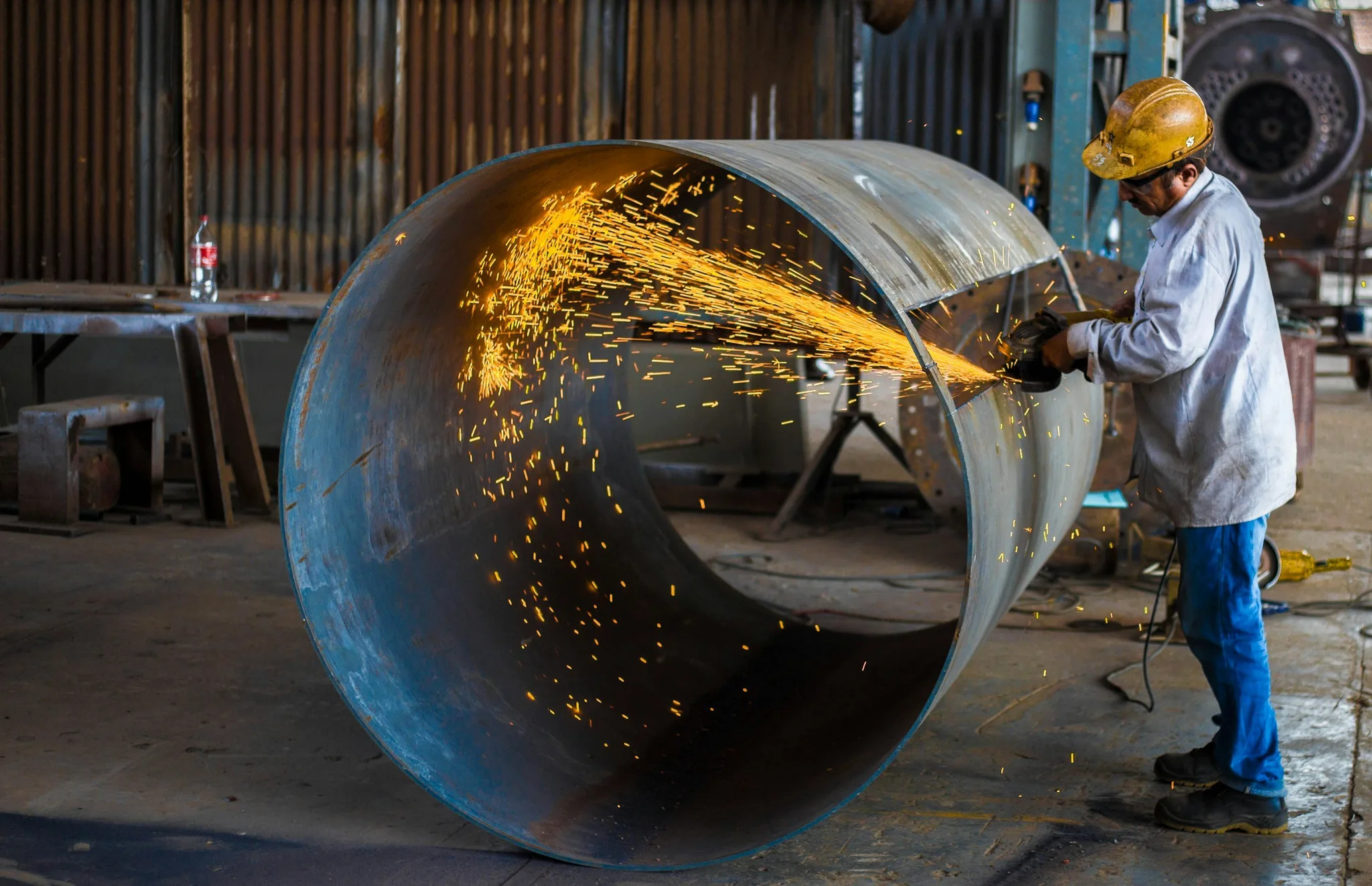 A worker cutting a metal tube in an industrial workshop.