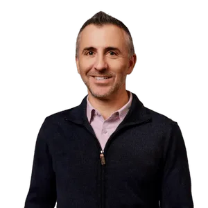 A smiling man in a dark sweater against a solid background.