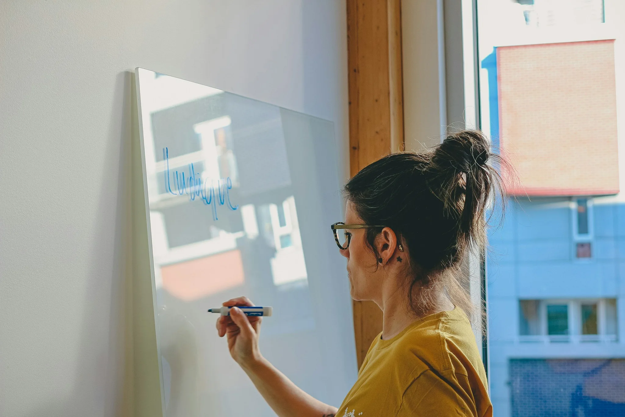 A woman writing on a clear whiteboard in a workspace.