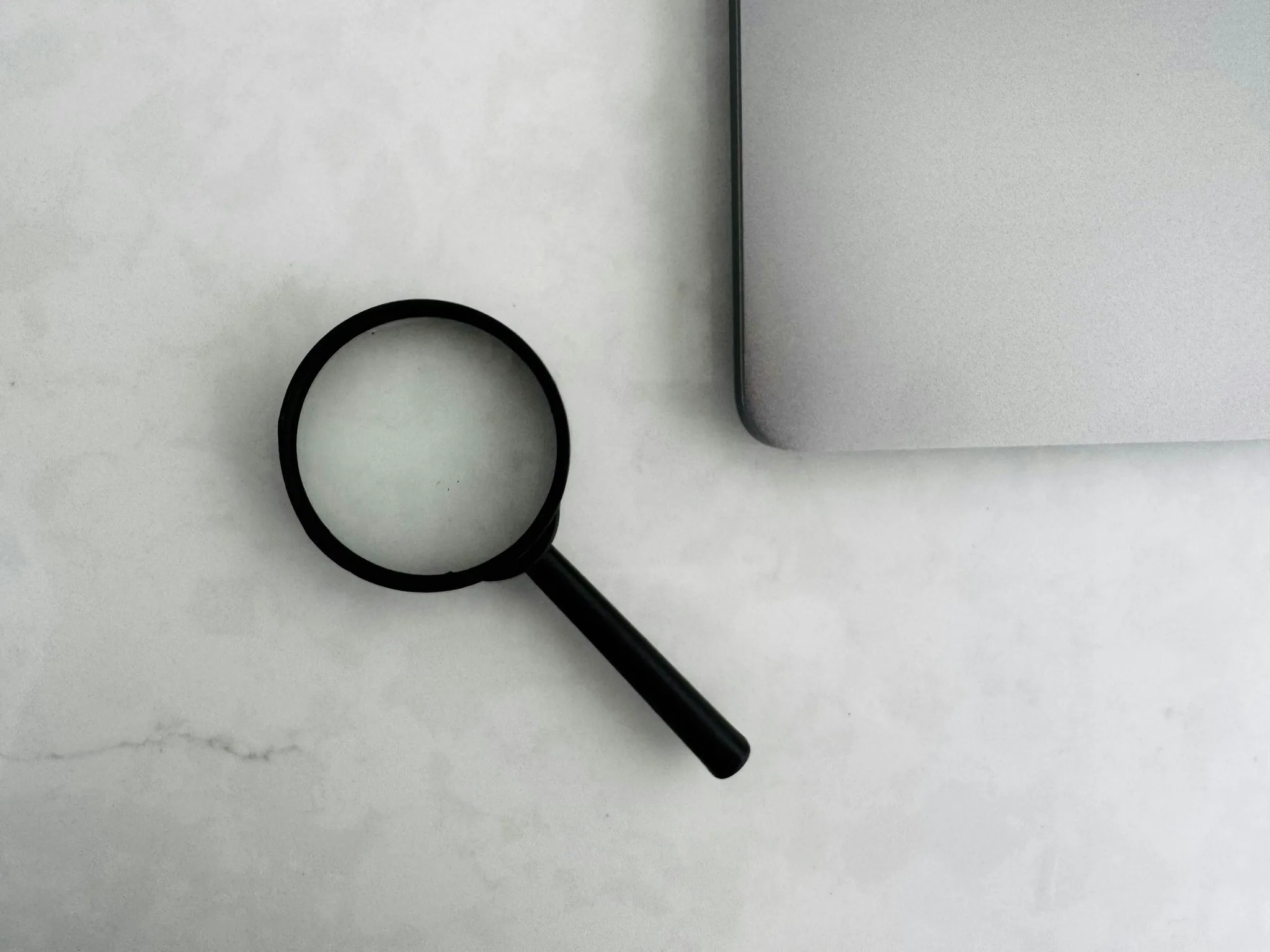 A magnifying glass on a marble surface next to a laptop.