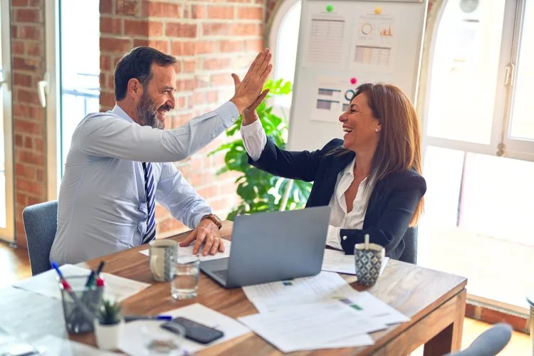 A man and woman high-fiving in an office setting.