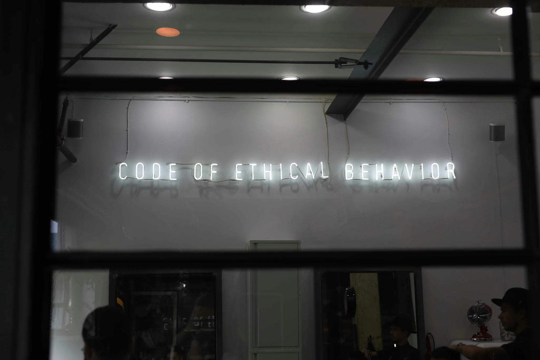 Neon sign reading 'CODE OF ETHICAL BEHAVIOR' on a white wall.