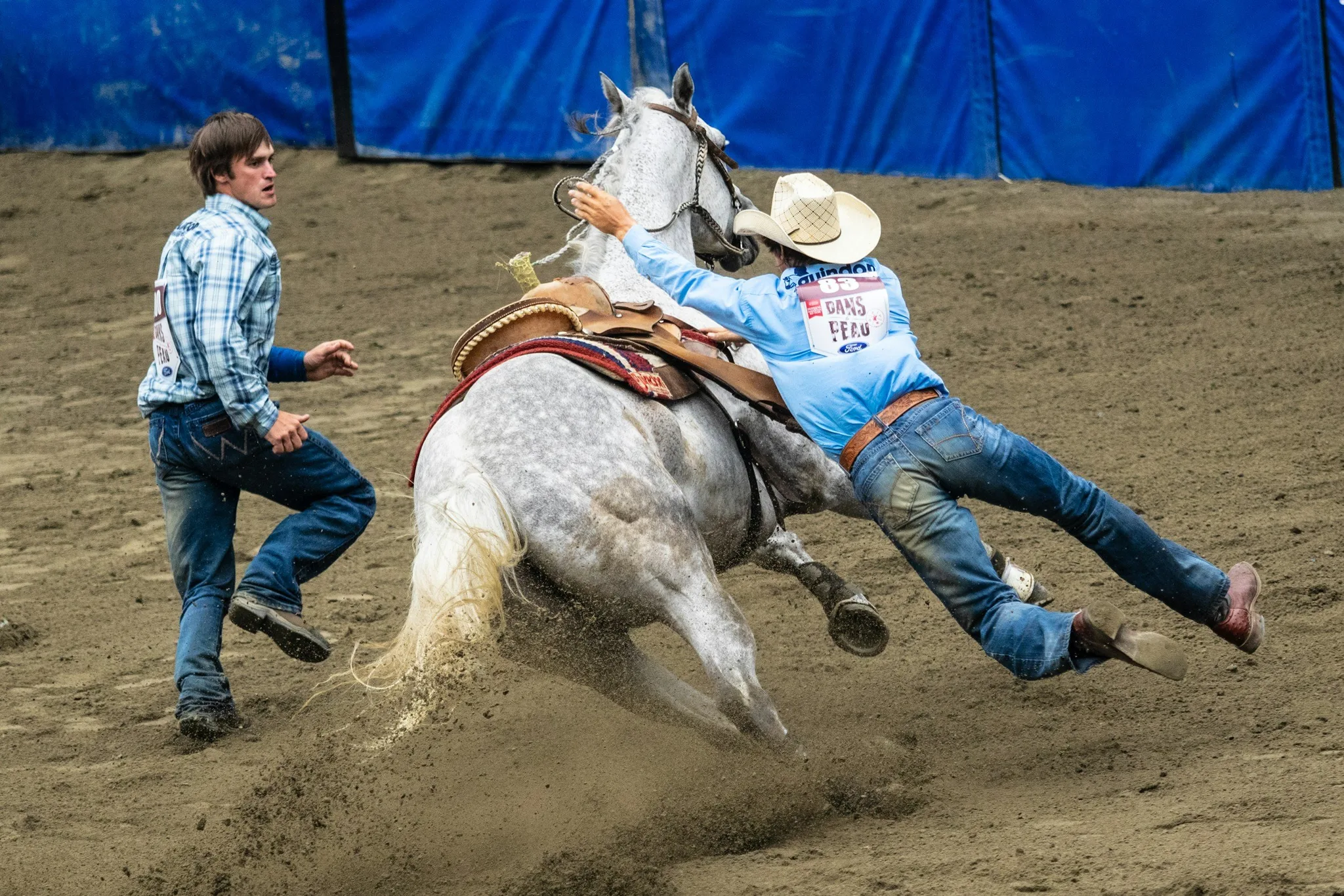 A cowboy riding a bucking gray horse at a rodeo event.