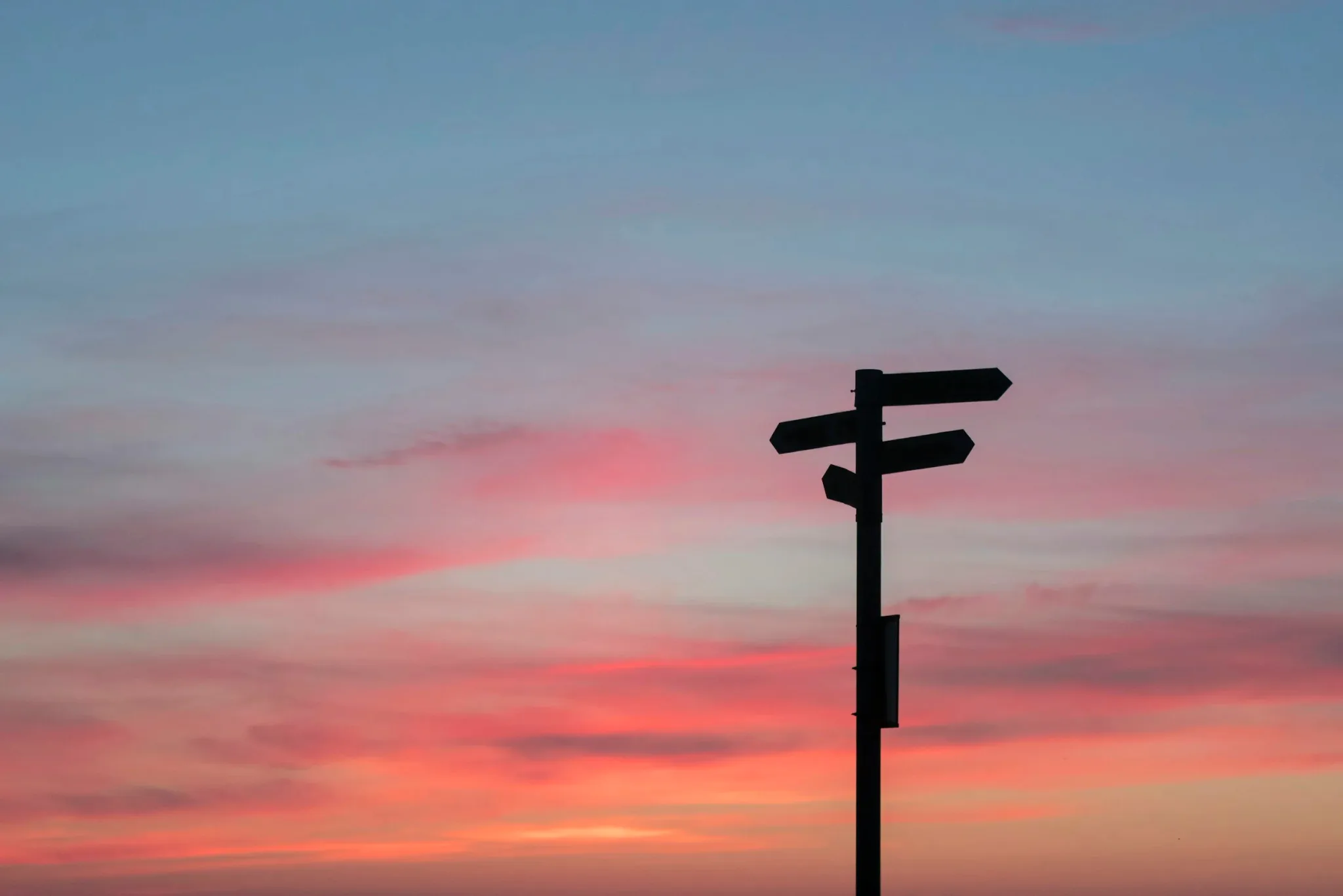 Silhouette of a signpost against a colorful sunset sky.